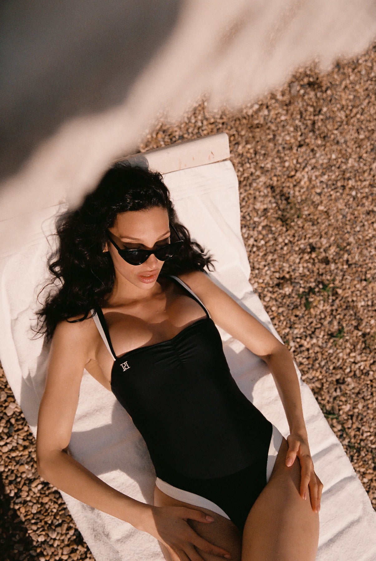 Monaco black ivory swimsuit/ one-piece with European swim fabric and 24 kt gold-plated hardware, view from the top of model on a sunbed